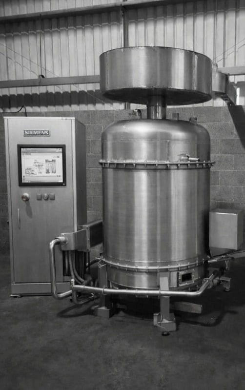 Black and white photograph of the Cyclonox stainless steel unit standing beside its control cabinet in a warehouse.