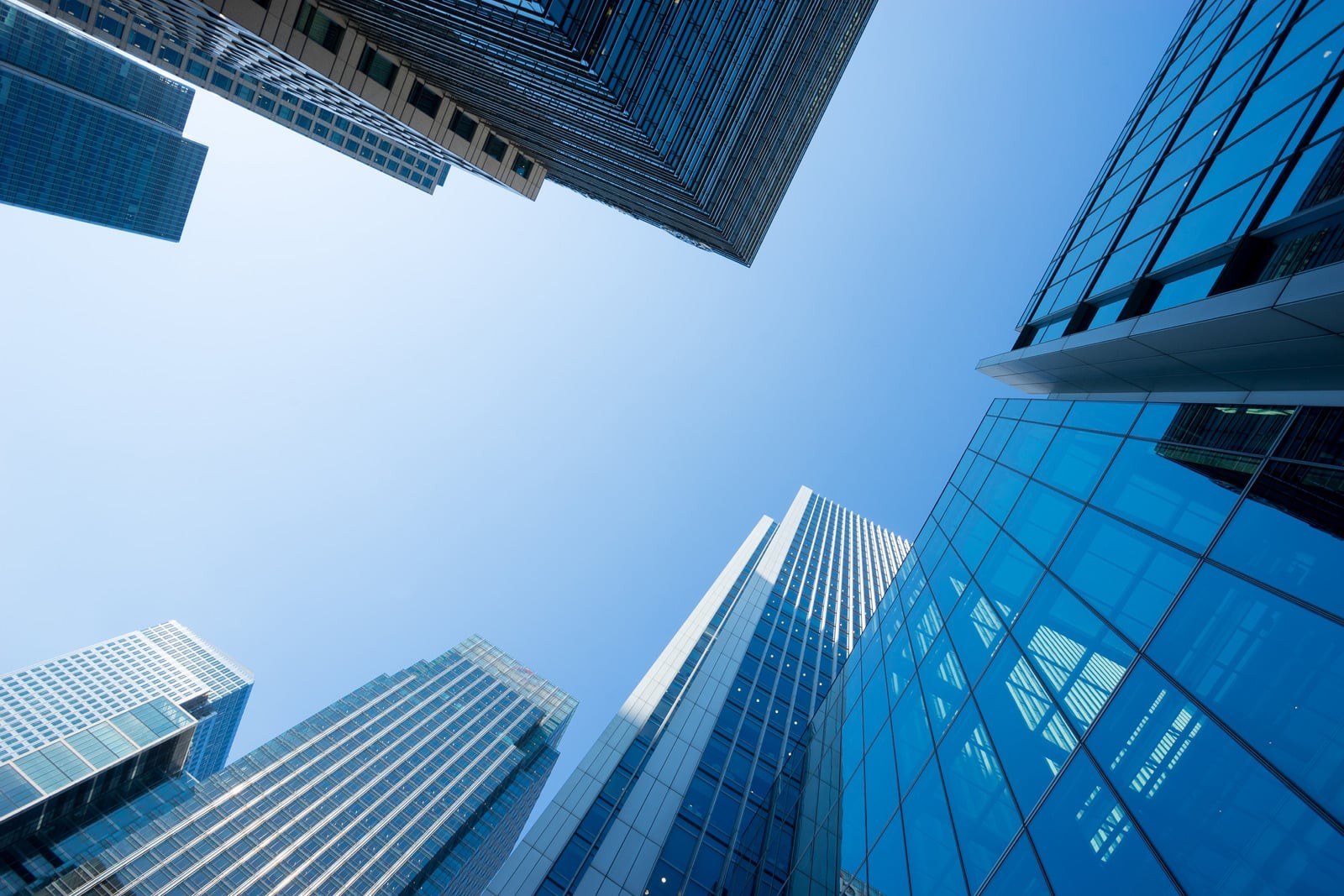 Looking up at glass and steel office towers against a clear blue sky.